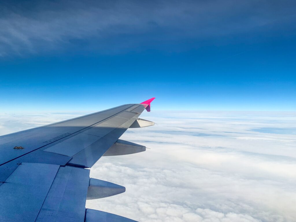 Aerial view of an airplane wing above clouds with clear blue sky, offering serene travel vibes.